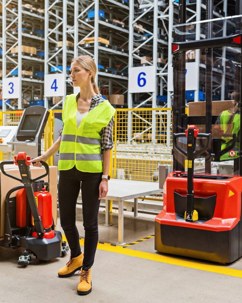 Caucasian employee working on modern warehouse. Industrial woman using reach truck with box